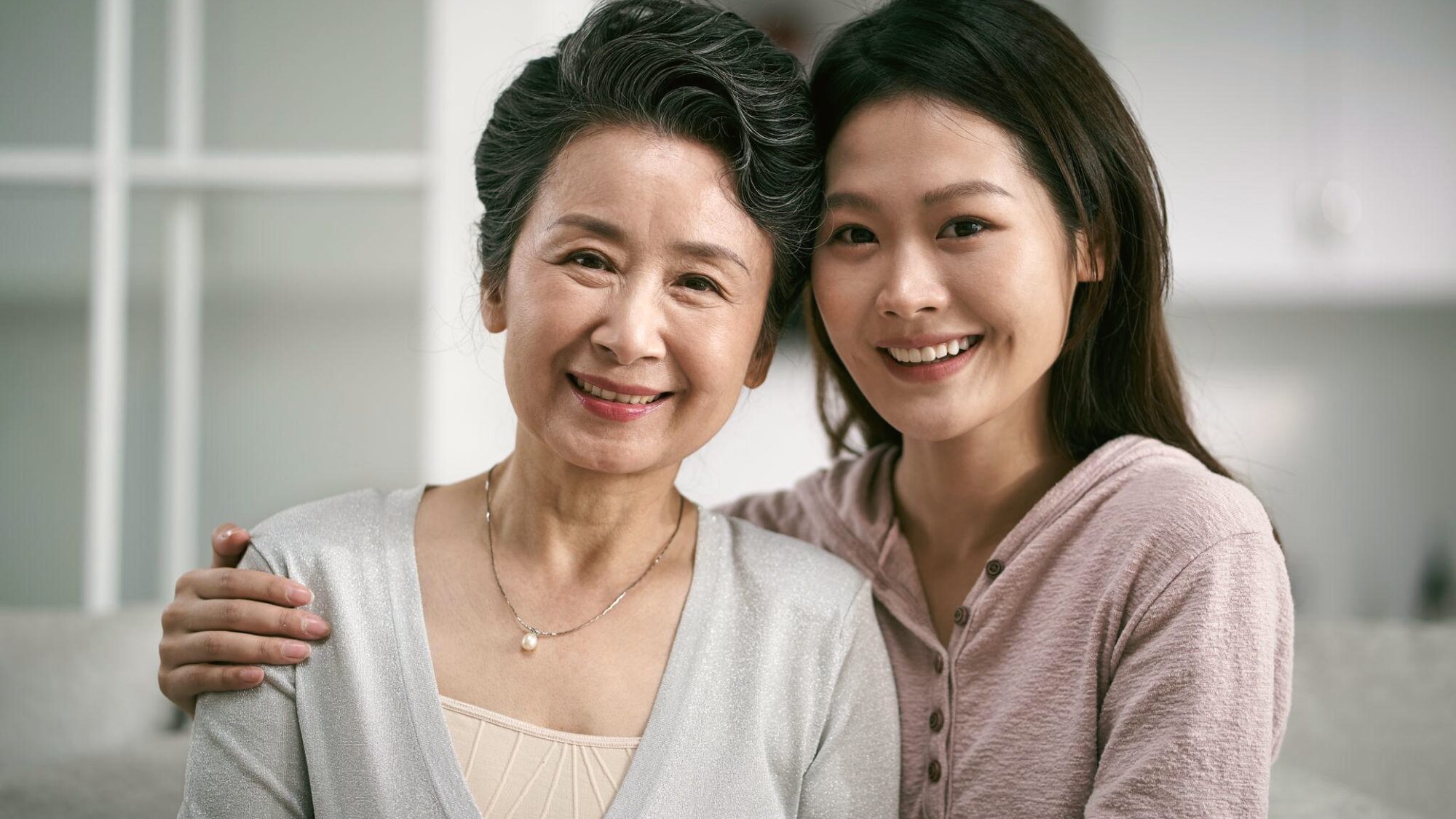 一位母亲和已经长大的女儿依偎在一起，对着镜头微笑（示意照片）
